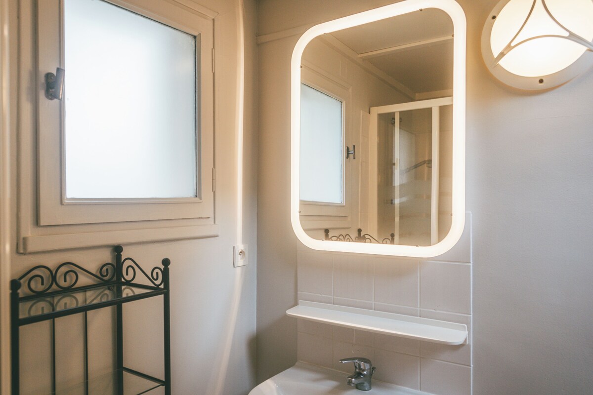 A bathroom with a white sink, a mirror with a light, and a window.