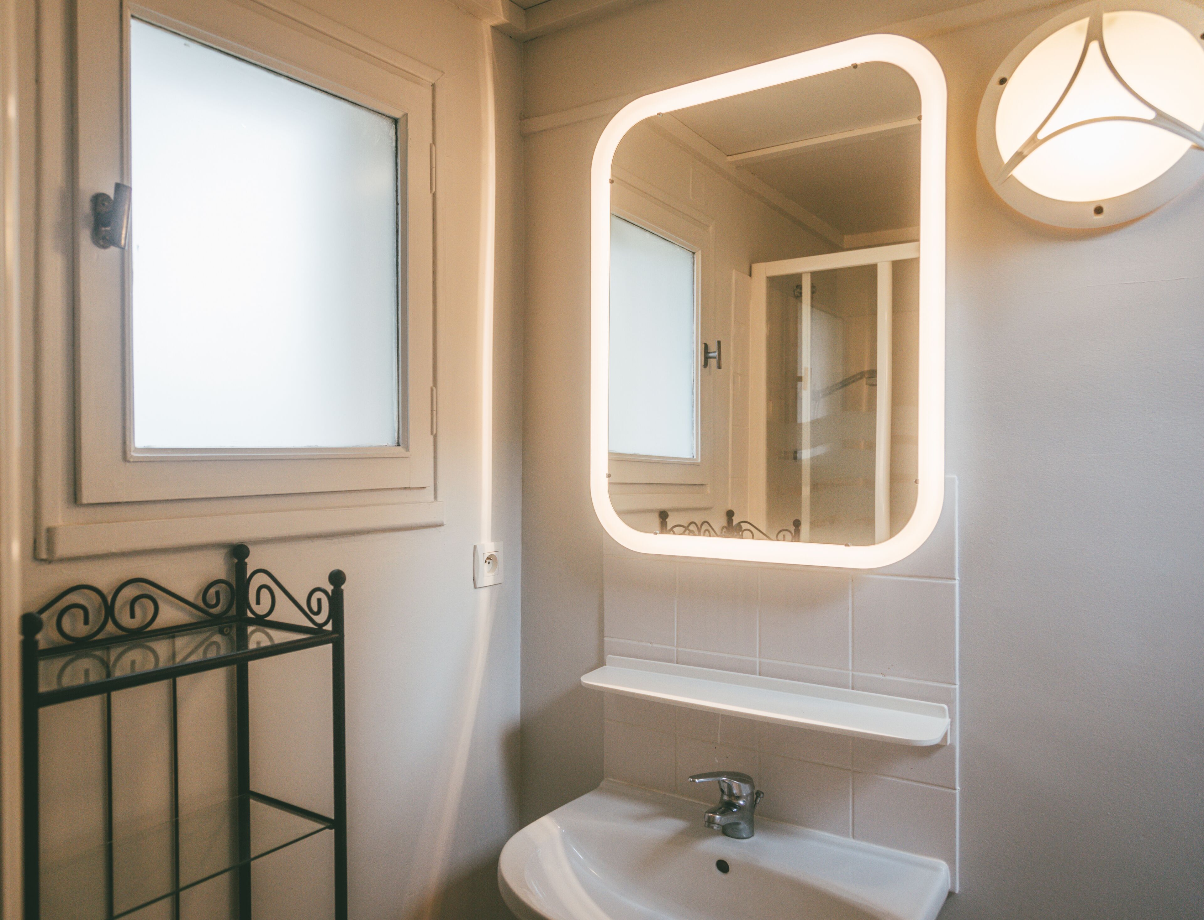 A bathroom with a white sink, a mirror with a light, and a window.