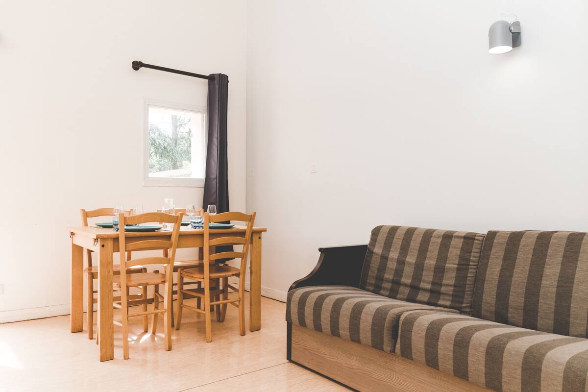 Ein gemütliches Wohnzimmer mit einem Holzespeisetisch, der für vier Personen gedeckt ist, einer gestreiften Couch und einem Fenster mit Vorhang.