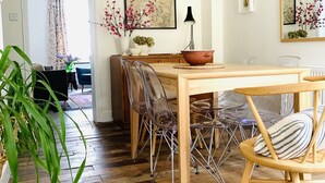Un coin repas avec une table en bois, des chaises en plastique transparent et un grand miroir au mur.