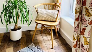 Une pièce d’angle avec une chaise en bois, une plante en pot, un tableau encadré au mur et des rideaux à motifs.