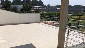 A rooftop terrace with a tiled floor, metal railing, and a view of surrounding buildings and greenery. - Bright, modern house with green views! (Lage)