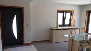 A modern kitchen with a glass dining table and chairs, a small cabinet, and a window with blinds. - Bright, modern house with green views! (Lage)