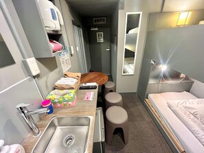 A compact hotel room with a bed, a small sink, a mirror, a bedside table, and a toilet. - Rhodes Otsuka Hotel - Hostel (Tokyo)