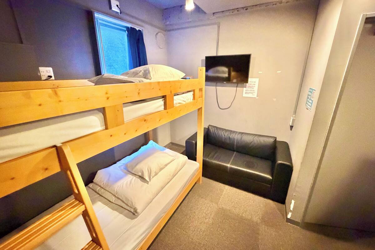 A room with bunk beds, a leather couch, a television, and a window with curtains.