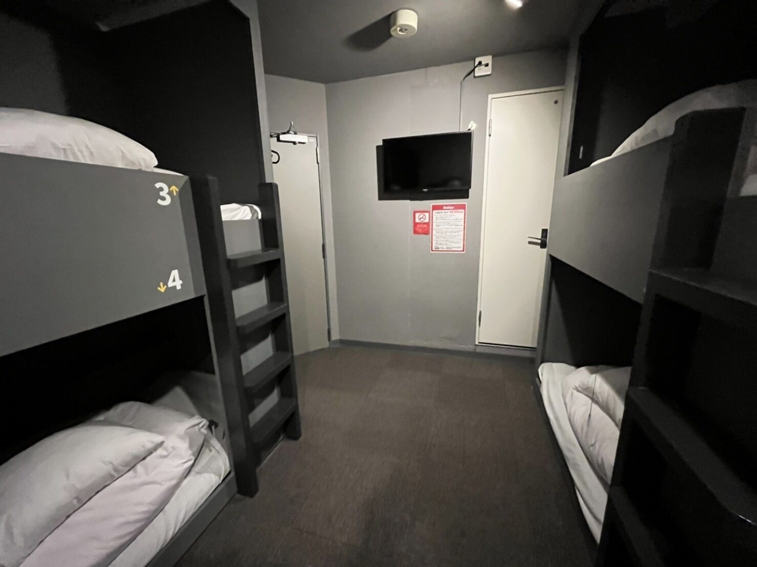 A dormitory room with bunk beds, a TV, a door, and a notice on the wall.