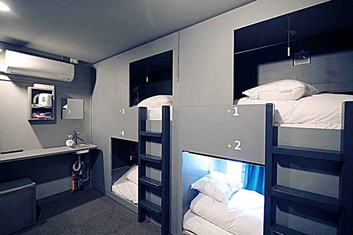 A dormitory room with bunk beds, a desk, a chair, a sink, and a mirror.