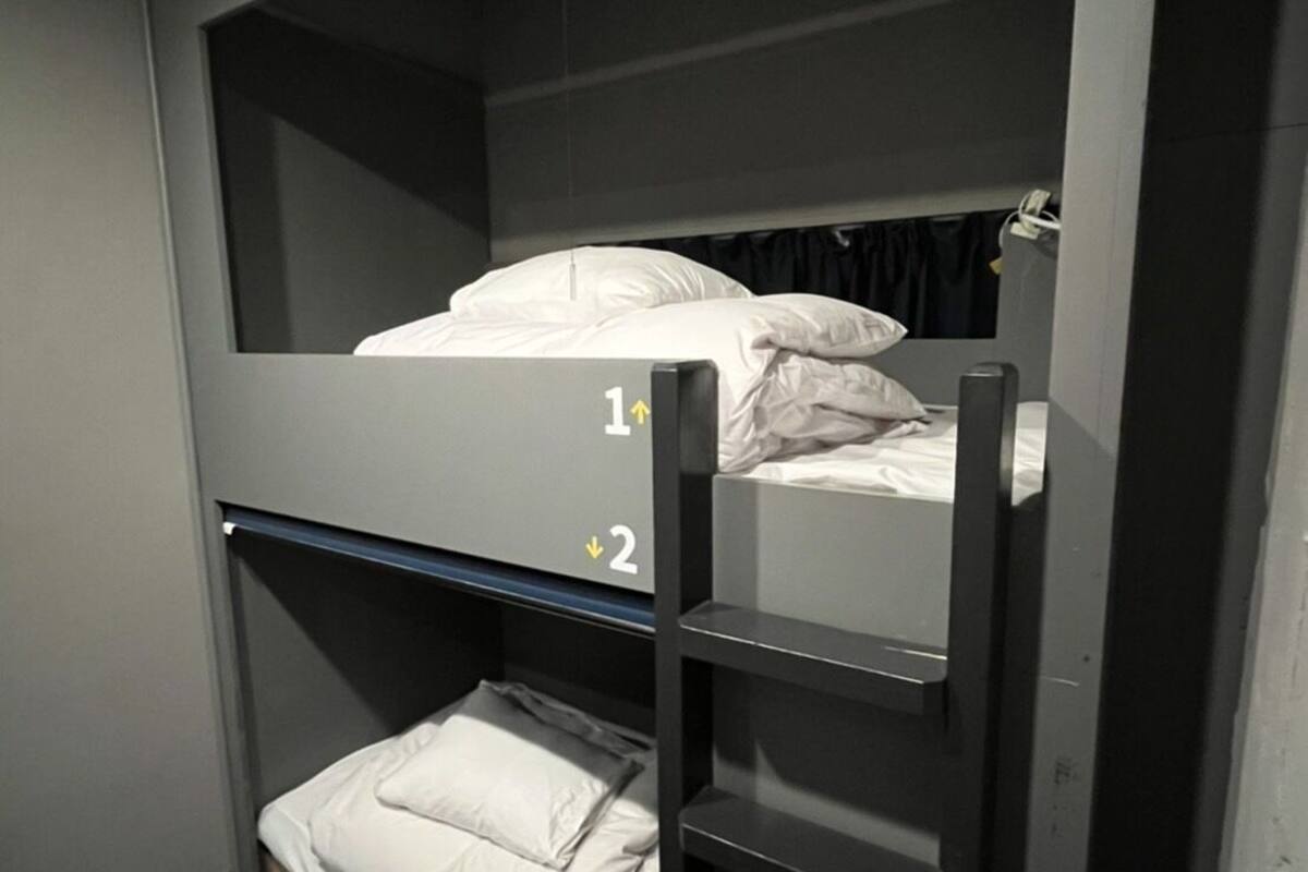 A bunk bed with two levels, each with a mattress and pillows. There is a ladder on the lower bunk.