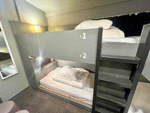 A bunk bed room with a ladder, a bedside table, and a wall-mounted lamp. - Rhodes Otsuka Hotel - Hostel (Tokyo)