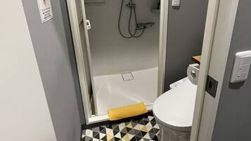 A narrow bathroom with a shower, toilet, and a patterned floor.