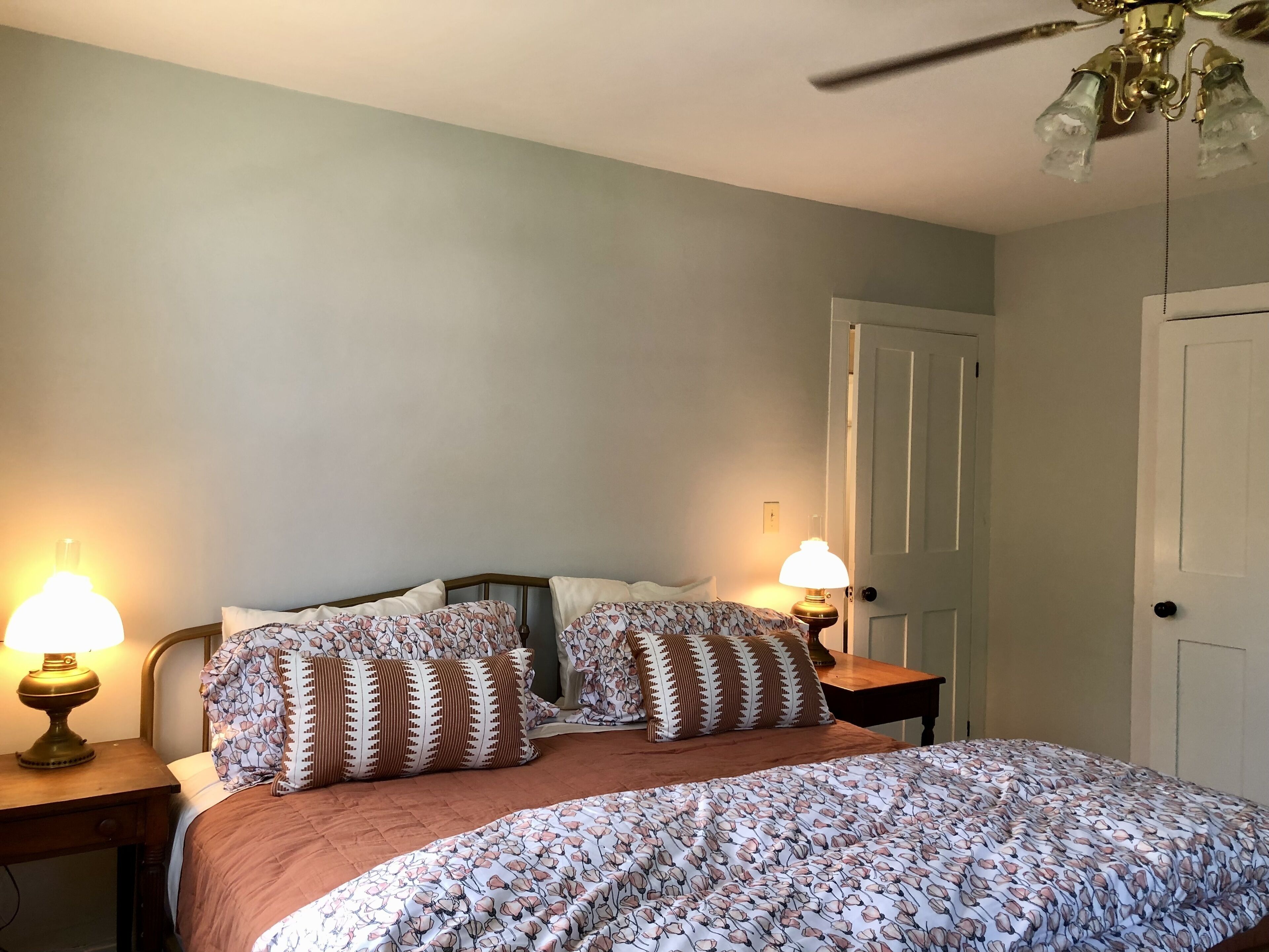 A bedroom with a bed, two bedside lamps, a ceiling fan, and a door.