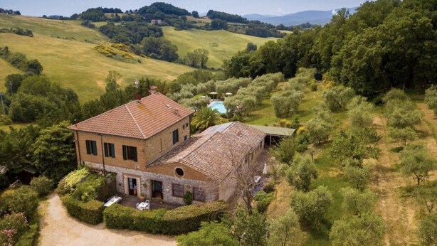 A large, two-story stone building with a tiled roof, surrounded by lush greenery and a clear blue sky. - GIRASOLE - IL VECCHIO MULINO TOSCANA (RADICONDOLI)