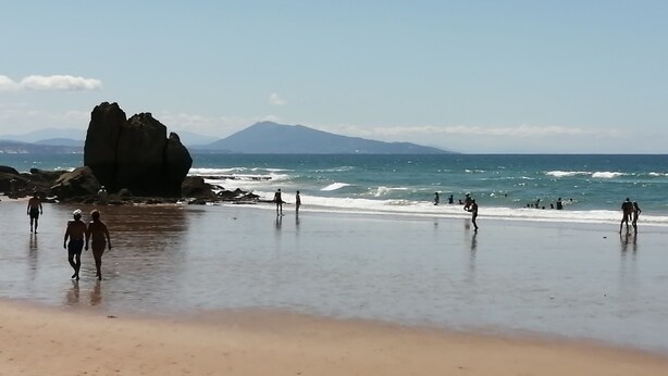 A beach with people walking and playing in the water, a large rock formation, and a mountain in the background. - Furnished studio Guéthary (basque coast)30m2-center village and beaches on foot **2023 (Guéthary)