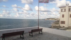 A stone-paved terrace with two wooden benches and a flagpole with a flag. - Furnished studio Guéthary (basque coast)30m2-center village and beaches on foot **2023 (Guéthary)