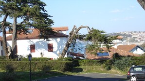 A residential street with a white house, a curved driveway, and a parked car. - Furnished studio Guéthary (basque coast)30m2-center village and beaches on foot **2023 (Guéthary)
