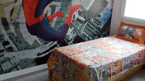 Ein Schlafzimmer mit einem Wandgemälde von Spider-Man, einem Bett mit bunter Bettdecke und einem Fenster mit Blick auf Gebäude.