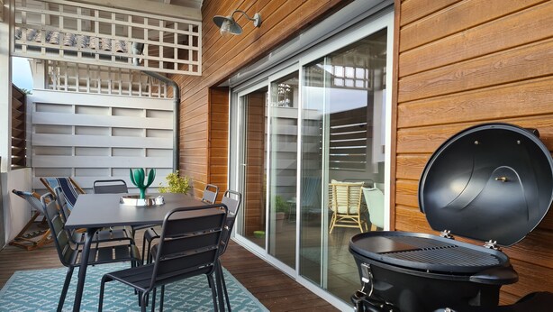 Eine Terrasse mit Tisch, Stühlen, einem Grill und einer Glasschiebetür, die zu einem Balkon führt.
