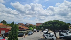 Eine Wohnstraße mit parkenden Autos, Häusern mit roten Ziegeldächern und einem klaren Himmel mit Wolken.