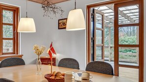 A dining area with a wooden table, two hanging pendant lights, a vase with flowers, a flag, and a basket of bread. - Pet friendly home in Videbæk with WiFi (Videbæk)
