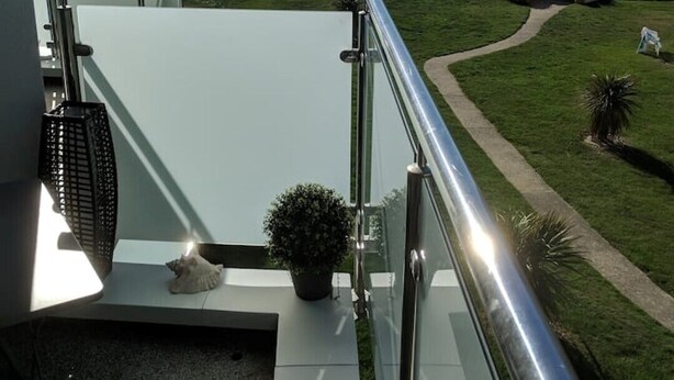 Un balcone con vista libera sul mare, una zona verdeggiante e un edificio moderno.