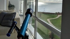 Un telescopio su un treppiede vicino a una grande finestra con vista su una zona erbosa e il mare.
