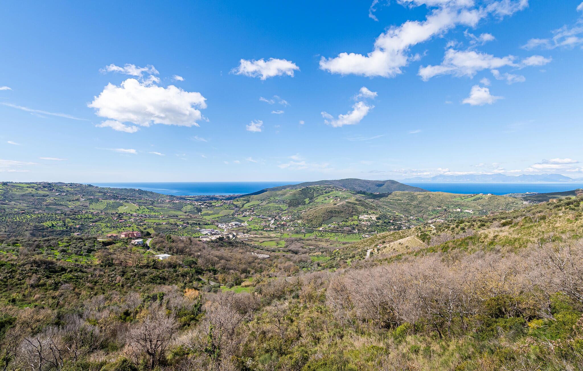 A panoramic view of a coastal landscape with rolling hills, scattered buildings, and a clear blue sky.