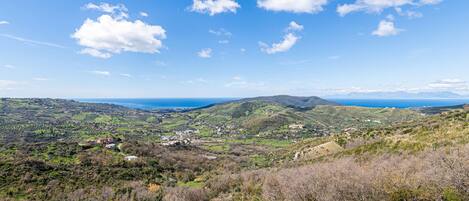 A panoramic view of a coastal landscape with rolling hills, scattered buildings, and a clear blue sky.