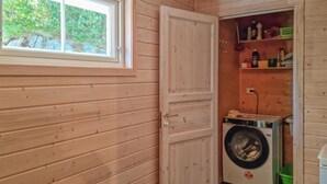 A laundry room with a washing machine, wooden walls, a window, and shelves with cleaning supplies.