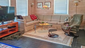 A cozy living room with a sectional sofa, a glass coffee table, a TV on a wooden stand, and a pet dog.