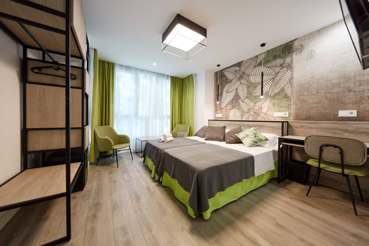 A modern hotel room with a bed, desk, chairs, and a large window with curtains.