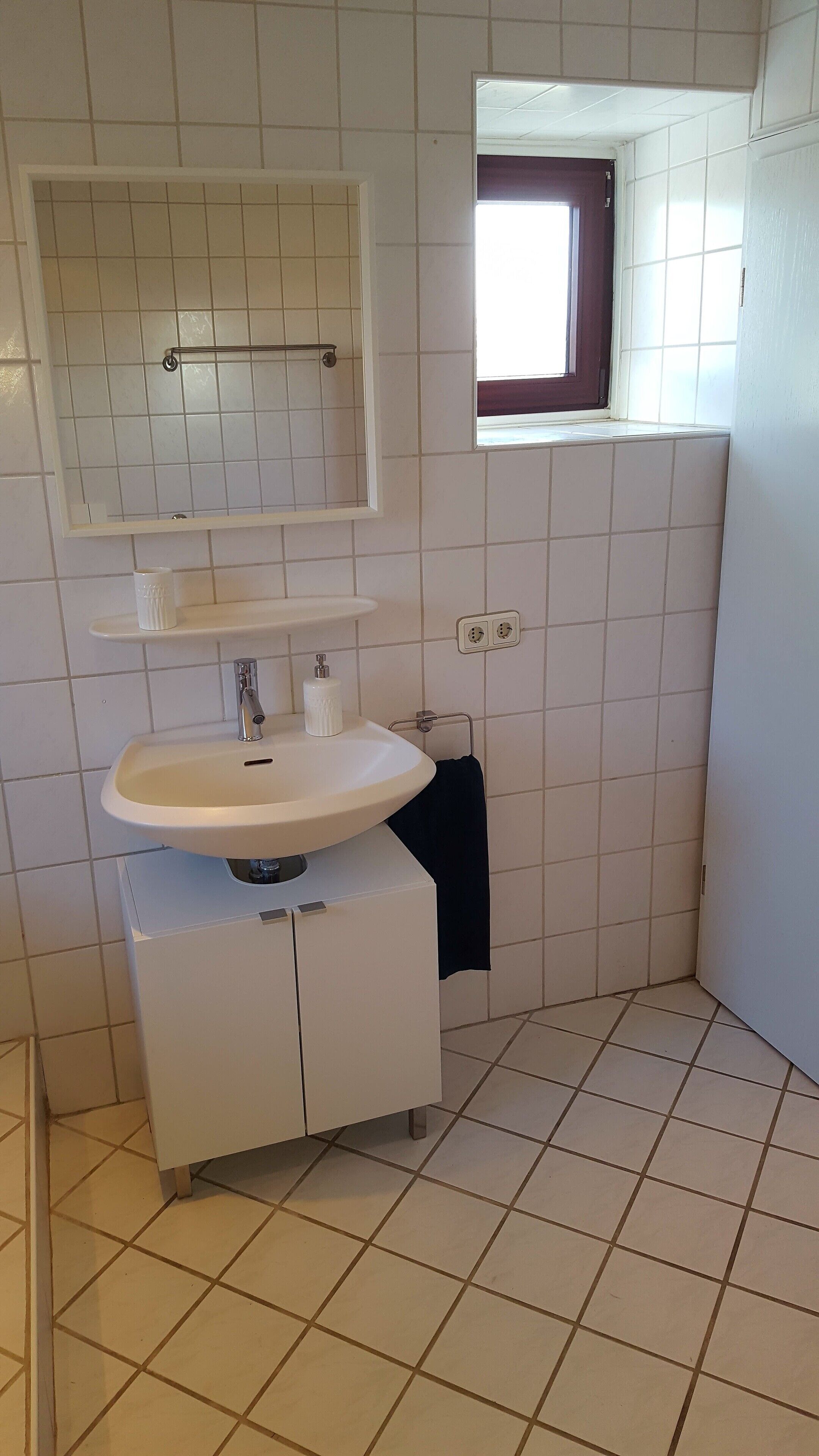 Ein kleines Badezimmer mit einem weißen Waschbecken, einem Spiegel und einem Fenster.