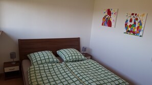 Ein Einzelbett mit Holz-Kopfteil, zwei Nachttische mit Lampen und zwei farbenfrohe Bilder an der Wand.
