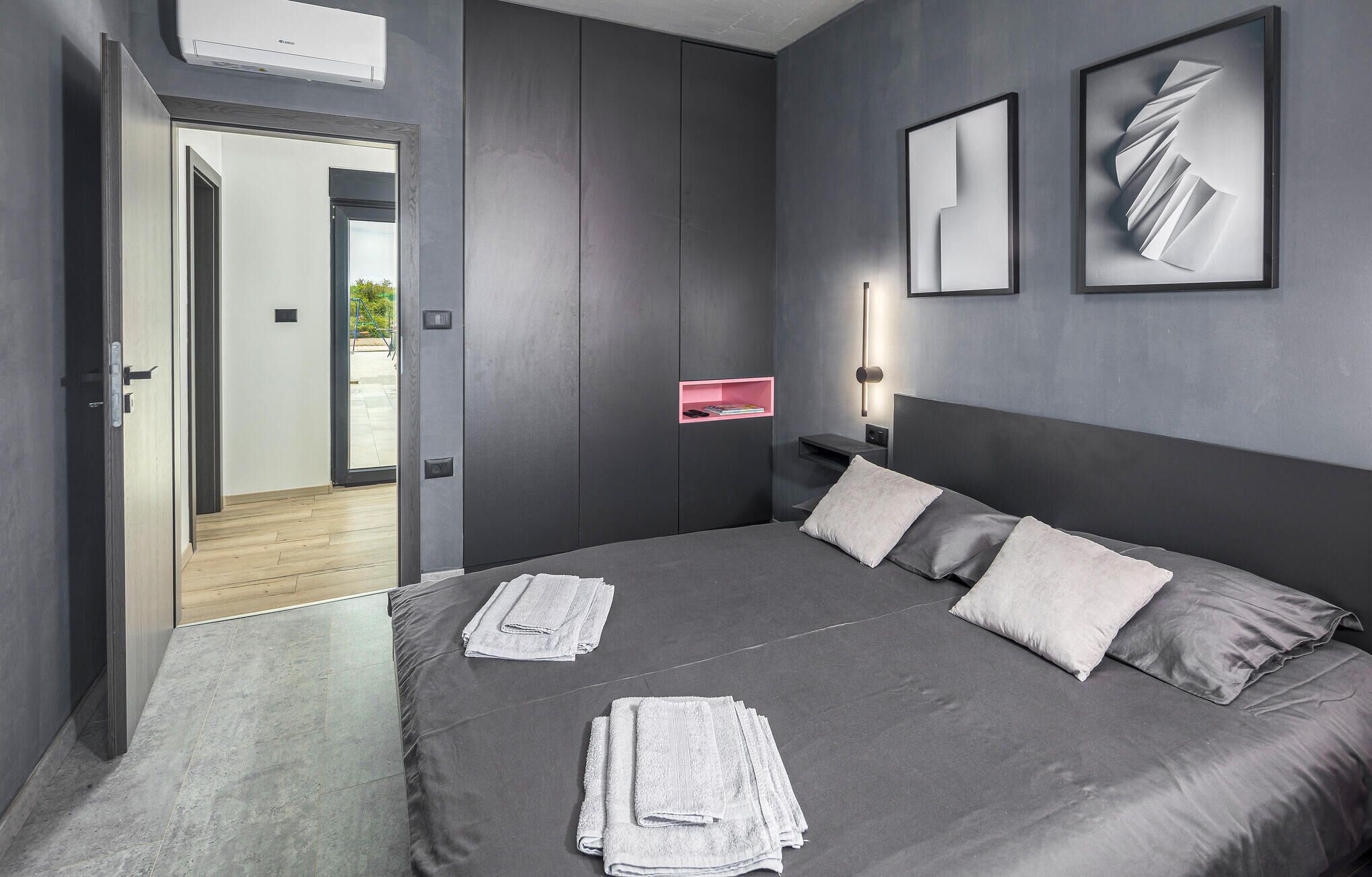 Une chambre à coucher moderne avec un grand lit, une porte donnant sur un balcon et deux œuvres d’art abstraites encadrées accrochées au mur.
