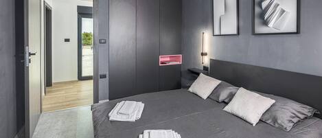 Une chambre à coucher moderne avec un grand lit, une porte donnant sur un balcon et deux œuvres d’art abstraites encadrées accrochées au mur.