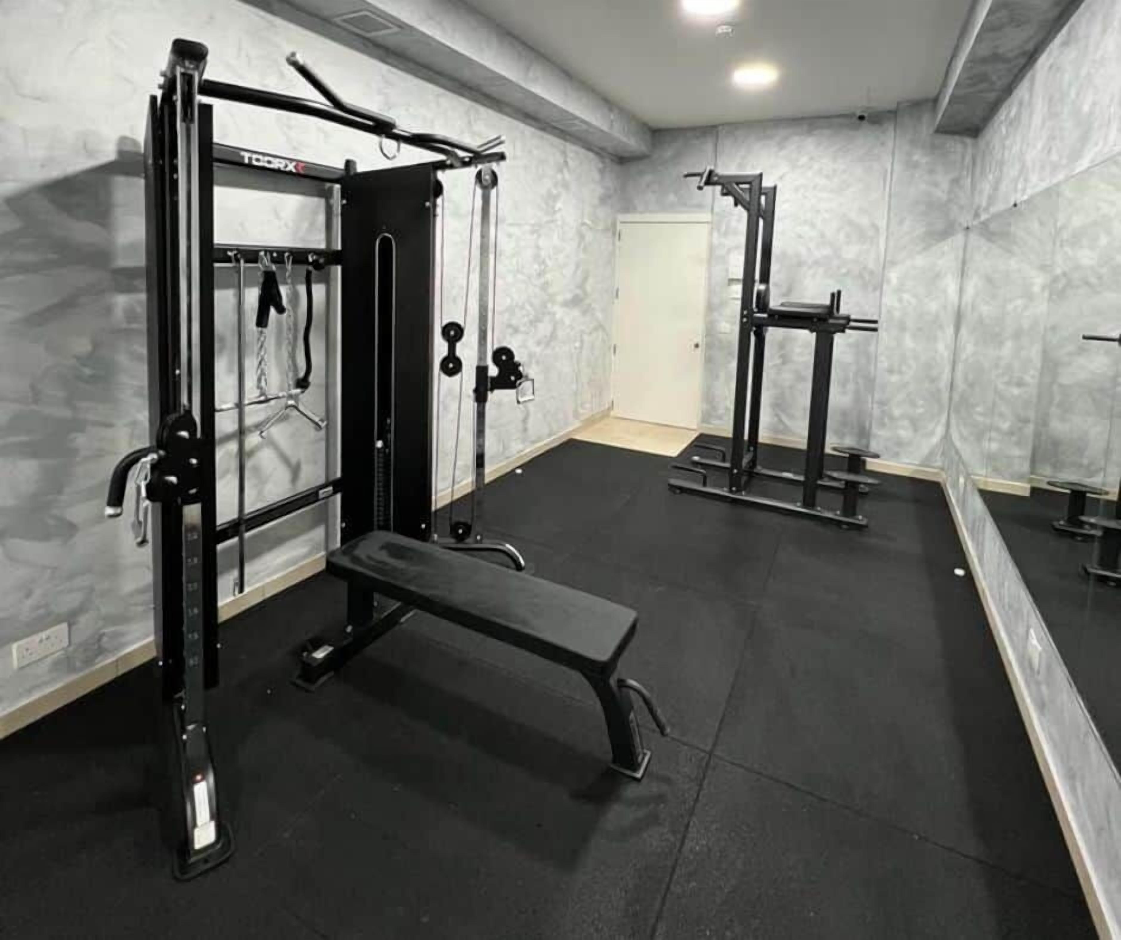 Une salle de sport équipée de matériel de musculation, d’un banc et d’un miroir.