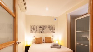 Quarto com cama, luminárias de cabeceira, ar condicionado fixado na parede e armário com portas deslizantes.