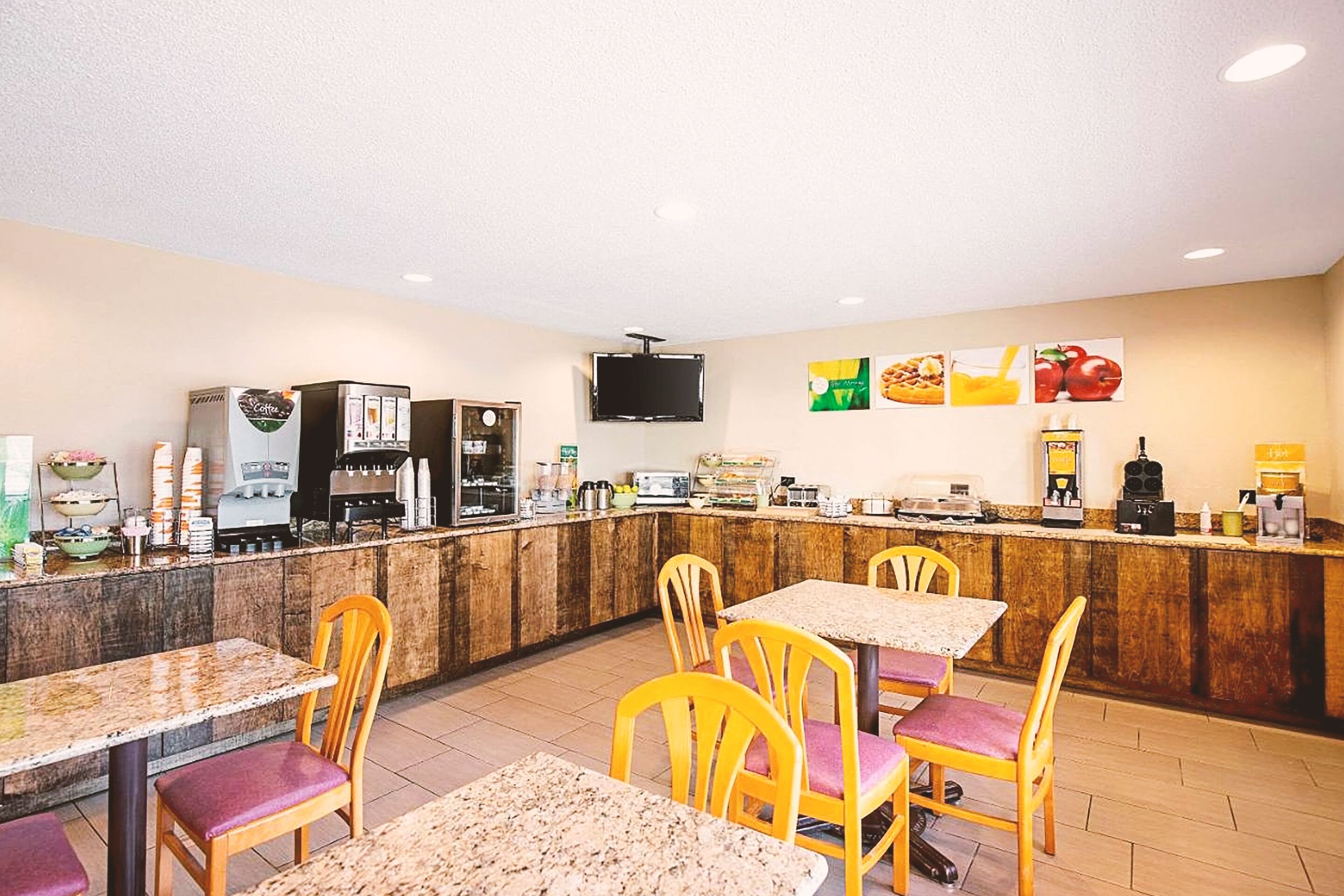 A restaurant with a counter, tables, chairs, and a television mounted on the wall.