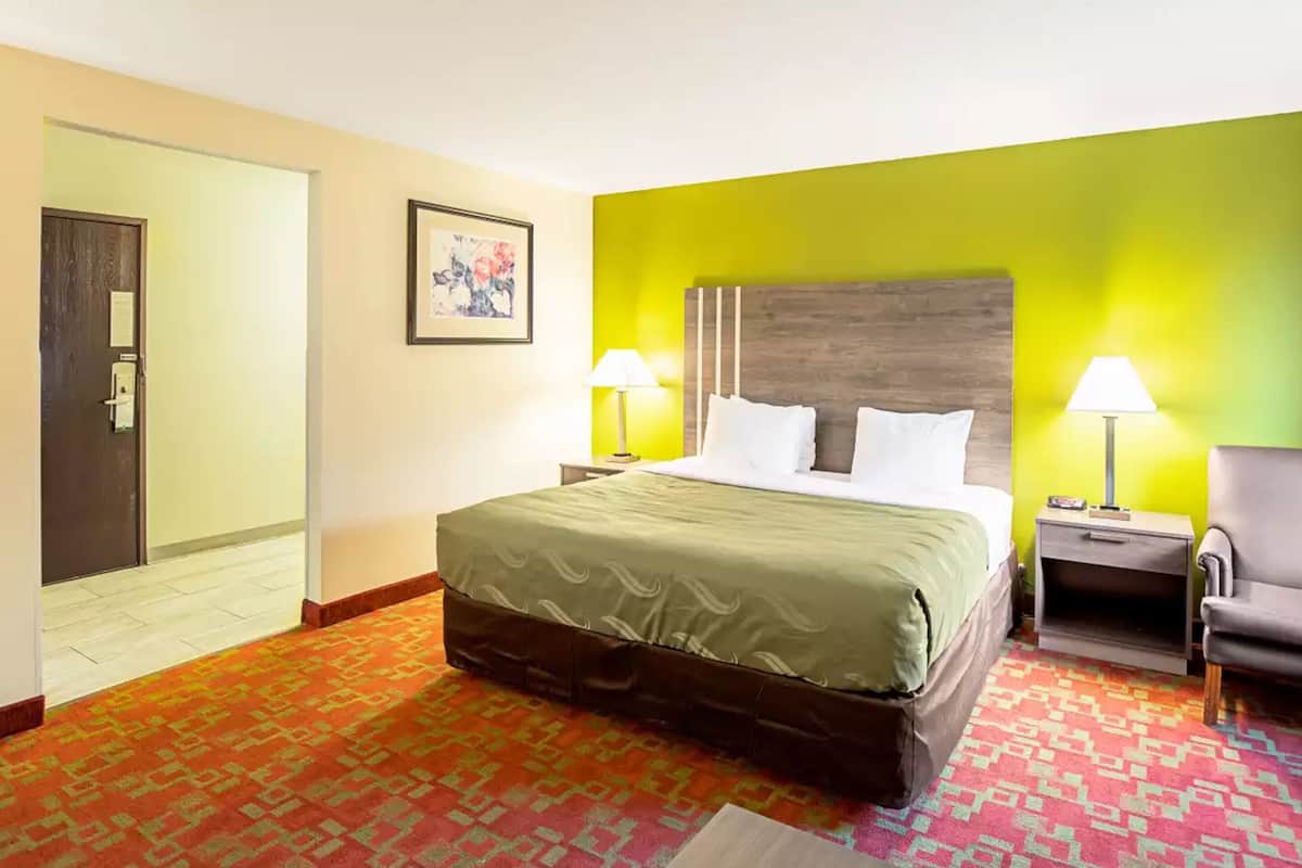 A hotel room with a bed, two bedside lamps, a chair, and a door.