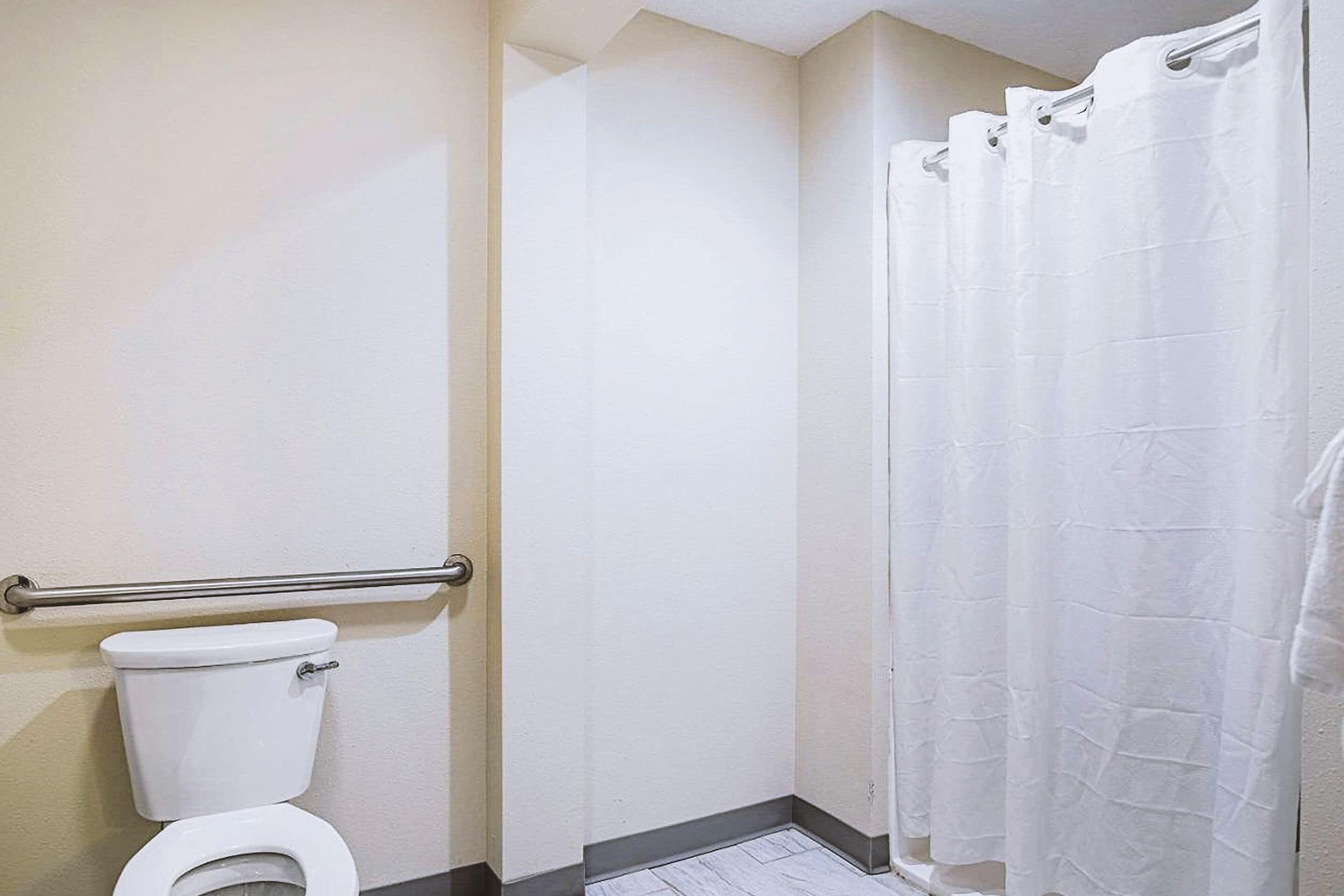 A bathroom with a white toilet, a shower curtain, and a grab bar.