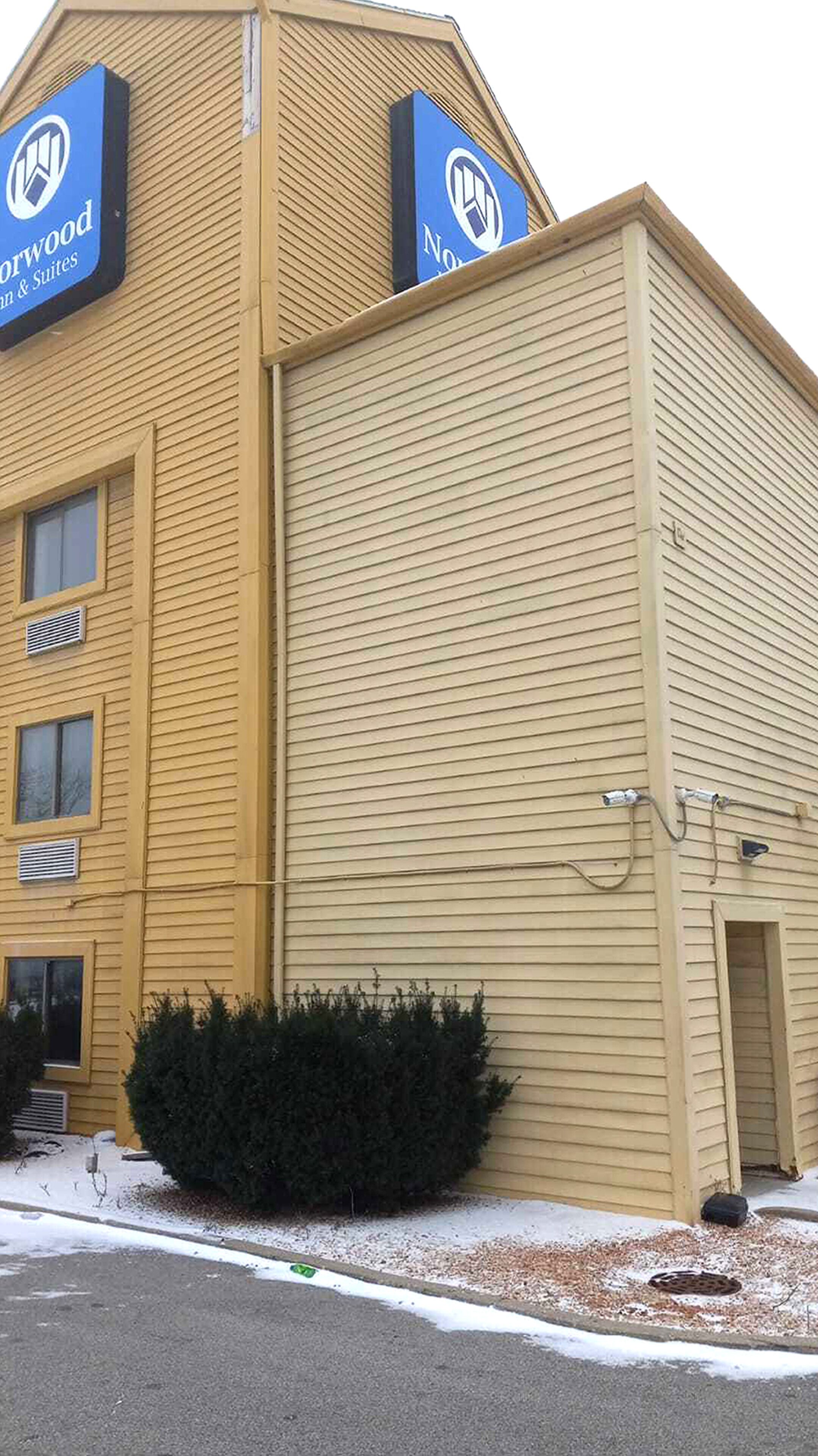 Un bâtiment à la façade jaune, orné de deux enseignes bleues avec des logos, et un petit arbuste devant l’entrée.