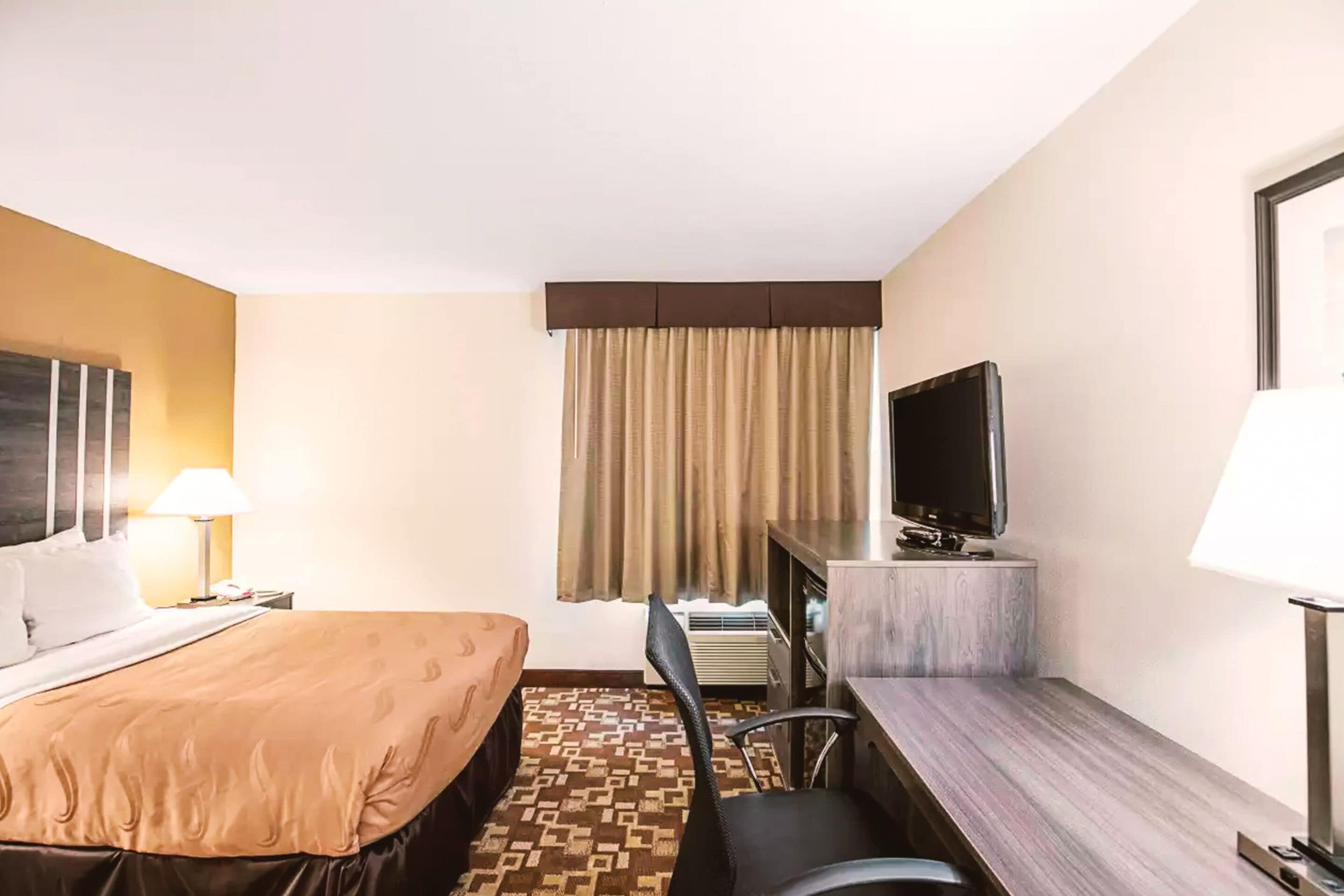A hotel room with a bed, a desk, a chair, a television, and a window with curtains.