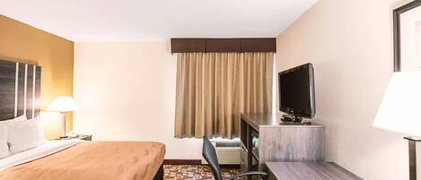 A hotel room with a bed, a desk, a chair, a television, and a window with curtains.