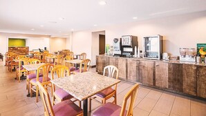 Ein Hotel-Essbereich mit mehreren Tischen und Stühlen, einer Kaffeestation und einer Theke mit verschiedenen Geräten.