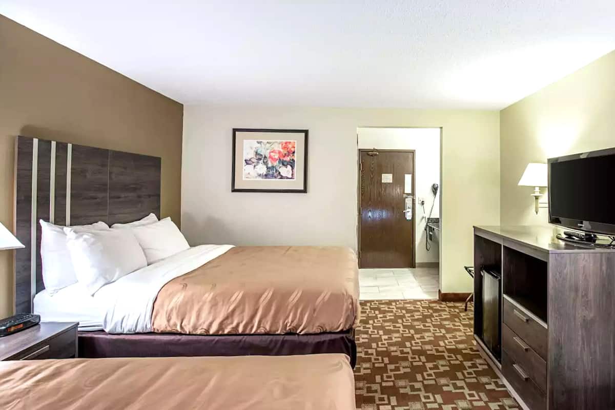 A hotel room with a large bed, a TV, a desk, and a door leading to the bathroom.