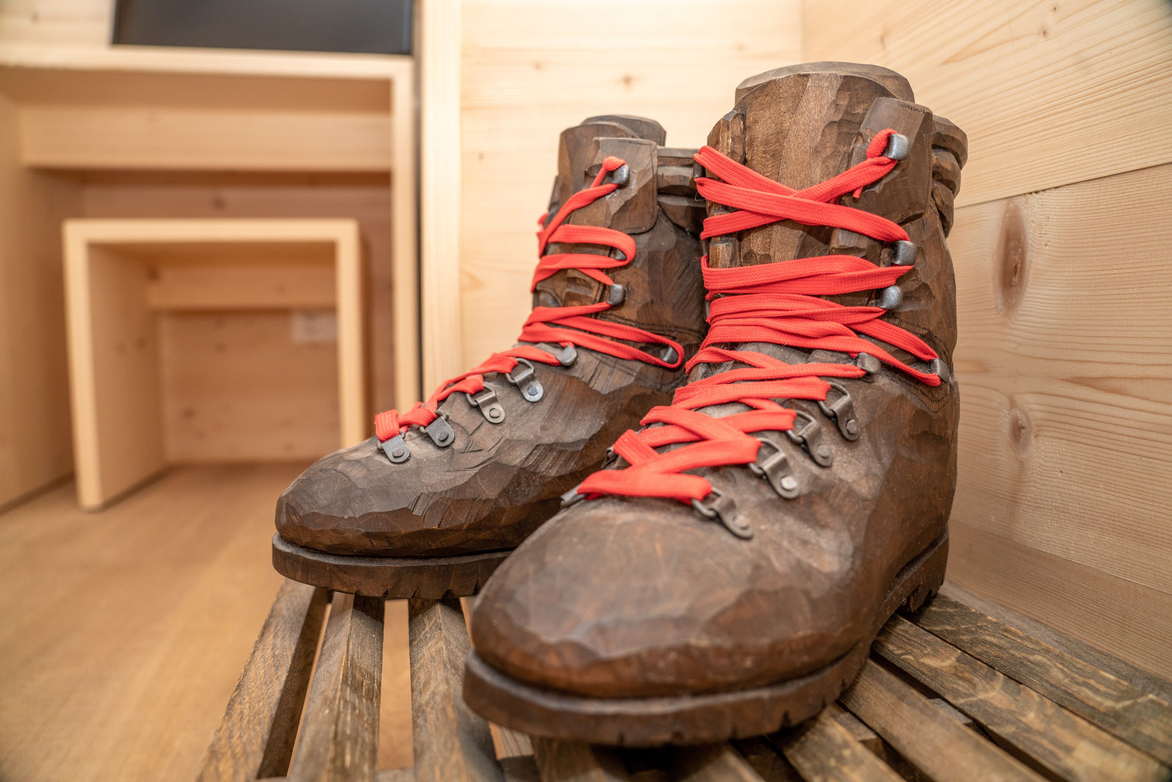 A pair of brown hiking boots with red laces on a wooden bench.