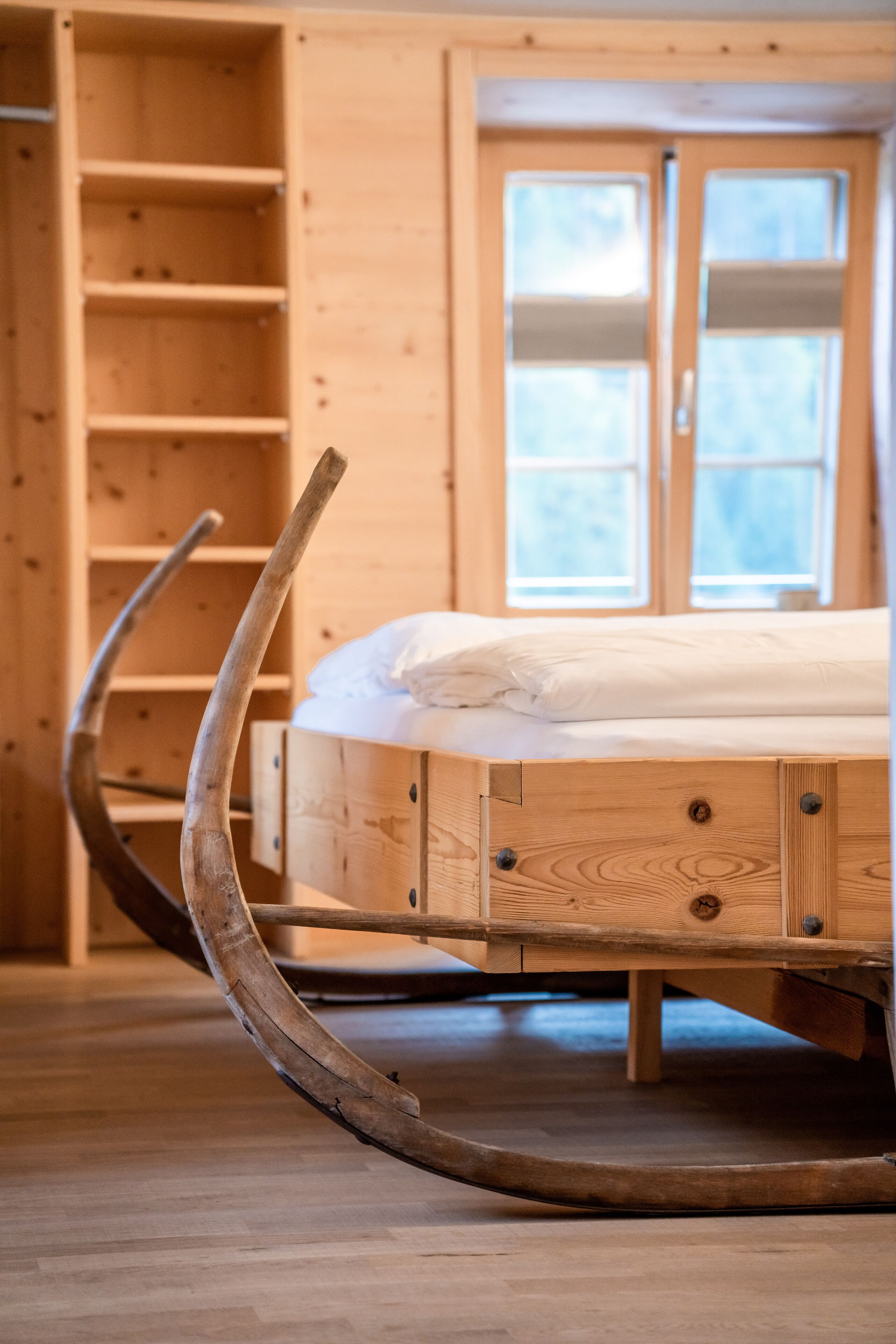 Una cama de madera con estructura metálica curvada, un armario de madera y una ventana con persianas.