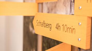 Ein hölzernes Wegweiser mit Pfeilen und Beschriftungen, die Entfernungen zu verschiedenen Orten angeben.