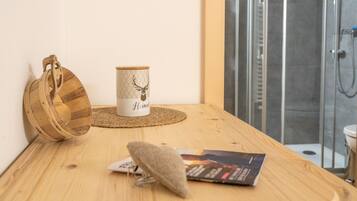 A wooden table with a woven placemat, a wooden bag, a mug with a deer design, and a magazine. A shower area is visible in the background.