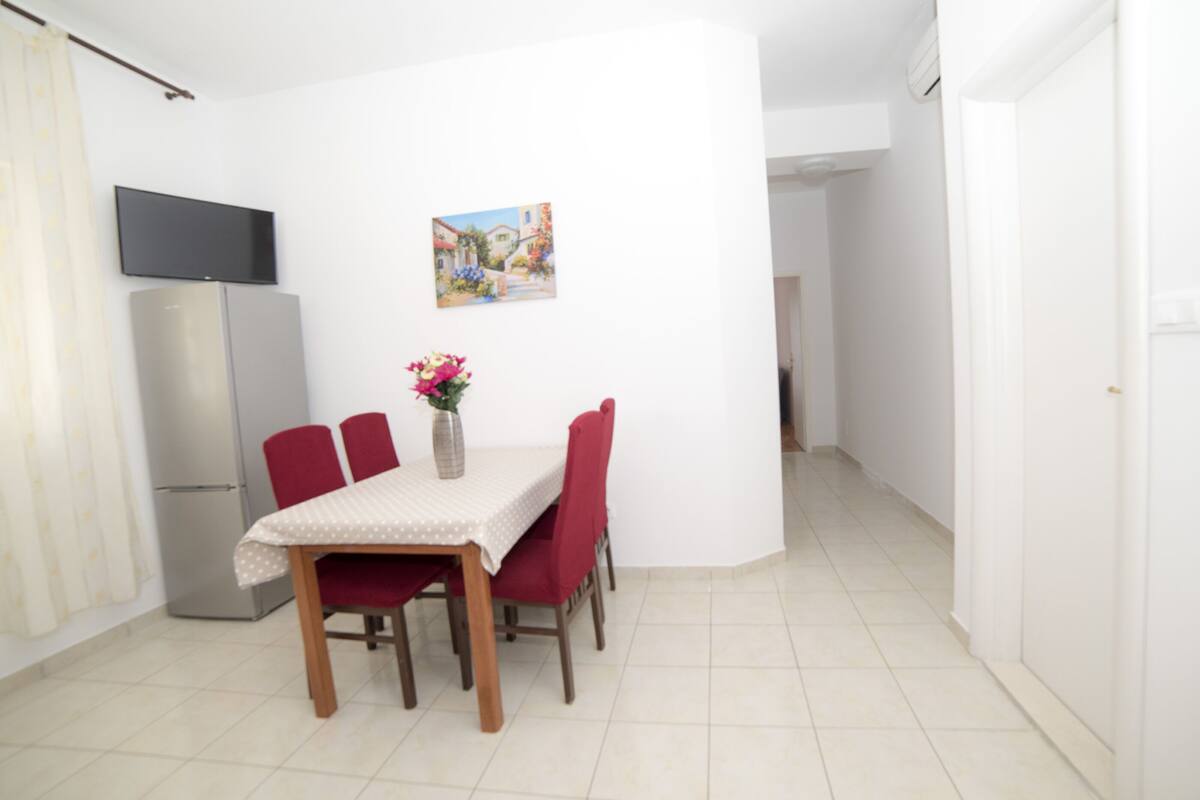 A dining area with a table, chairs, a refrigerator, and a painting on the wall.