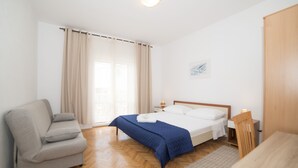 A bedroom with a bed, a sofa, a wooden table, and a window with curtains. - Apartments Pavla i Niko (Lokva Rogoznica)